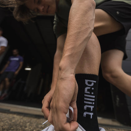 Teenage boy bending down to adjust his shoelaces, showcasing black socks with white Bullitt logo